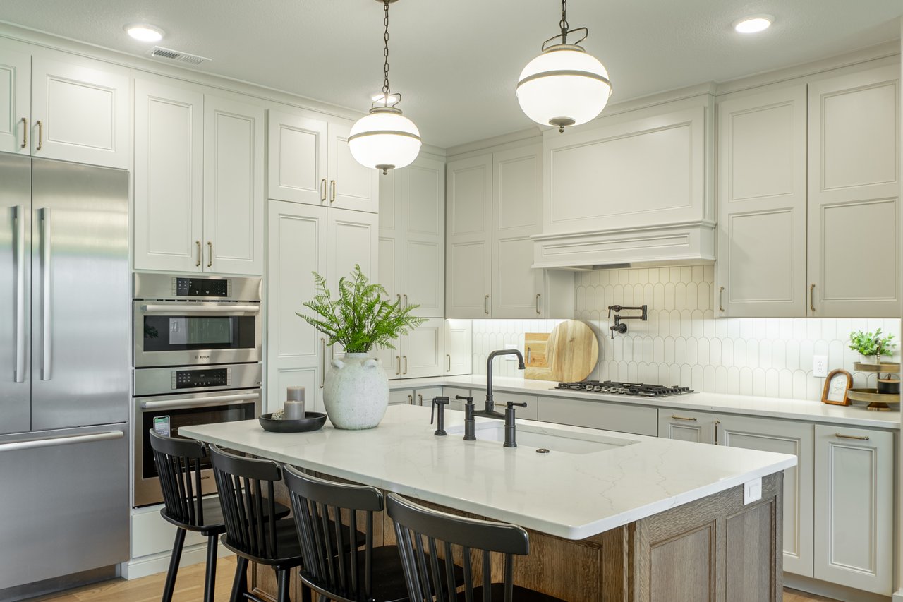 Bright kitchen with a large white island, paneled cabinets, stainless steel appliances, and globe pendant lights.