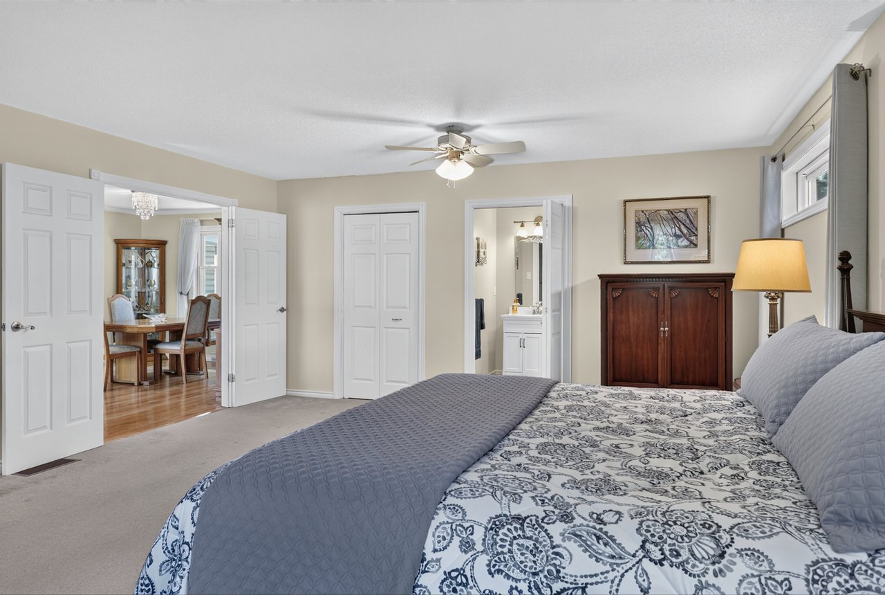 Bedroom with a patterned bedspread, wooden cabinet, and open doors to a bathroom and dining room.