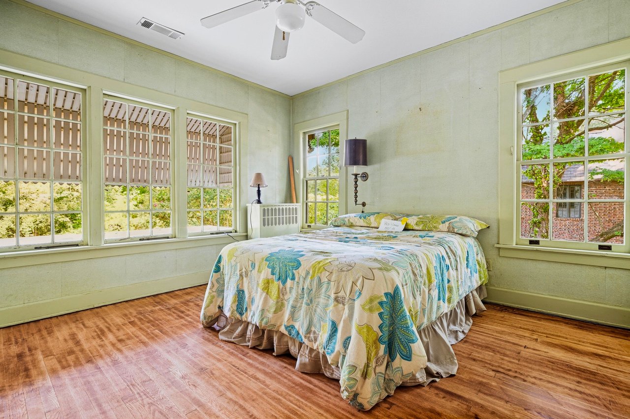 Bedroom with a colorful patterned bedspread and large windows overlooking trees.