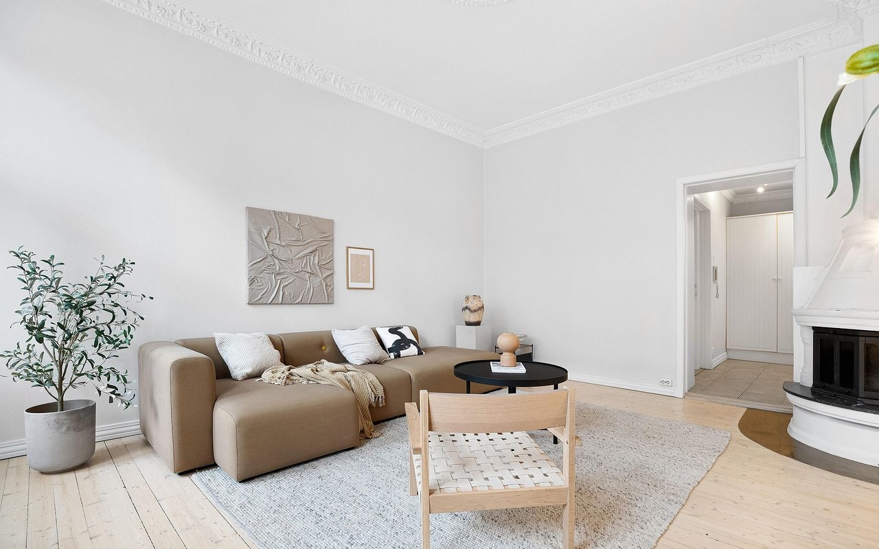 Living room with a beige sectional, pale wood floors, and a white fireplace.