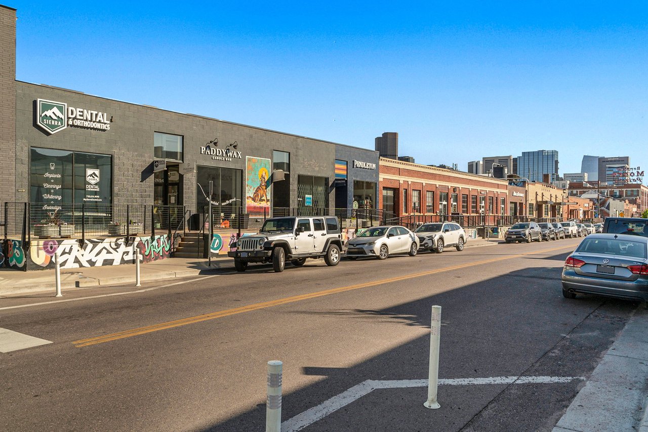 Commercial storefronts and street parking along a main road near Westgold Meadows in Arvada, Denver, CO.