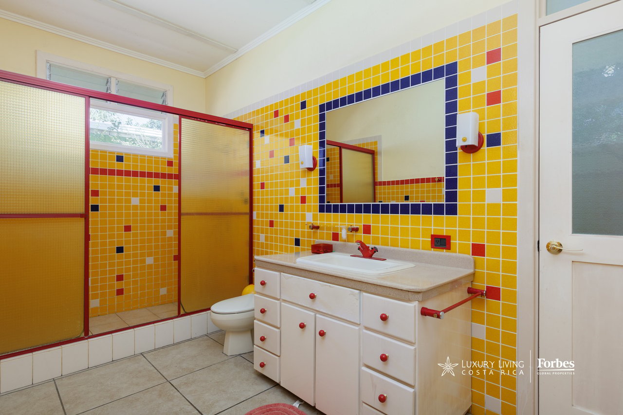 Bathroom with vivid yellow mosaic tile, red-trimmed shower, and white vanity.