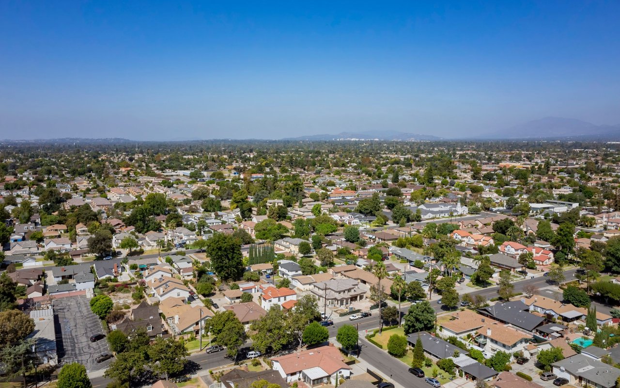 Aerial view of a suburban neighborhood with tree-lined streets and distant hills.