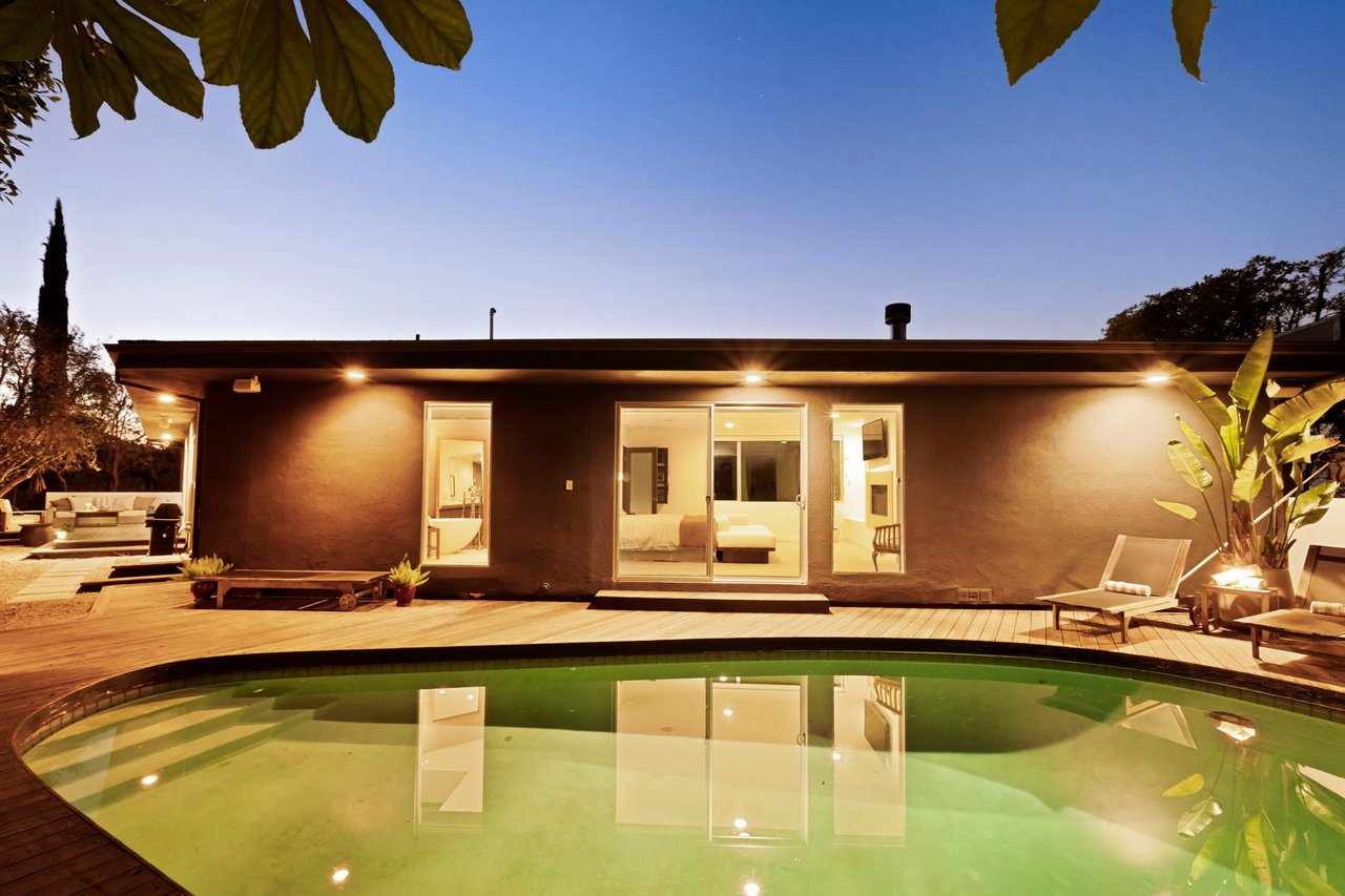 Modern home with a glowing backyard deck and swimming pool at dusk.