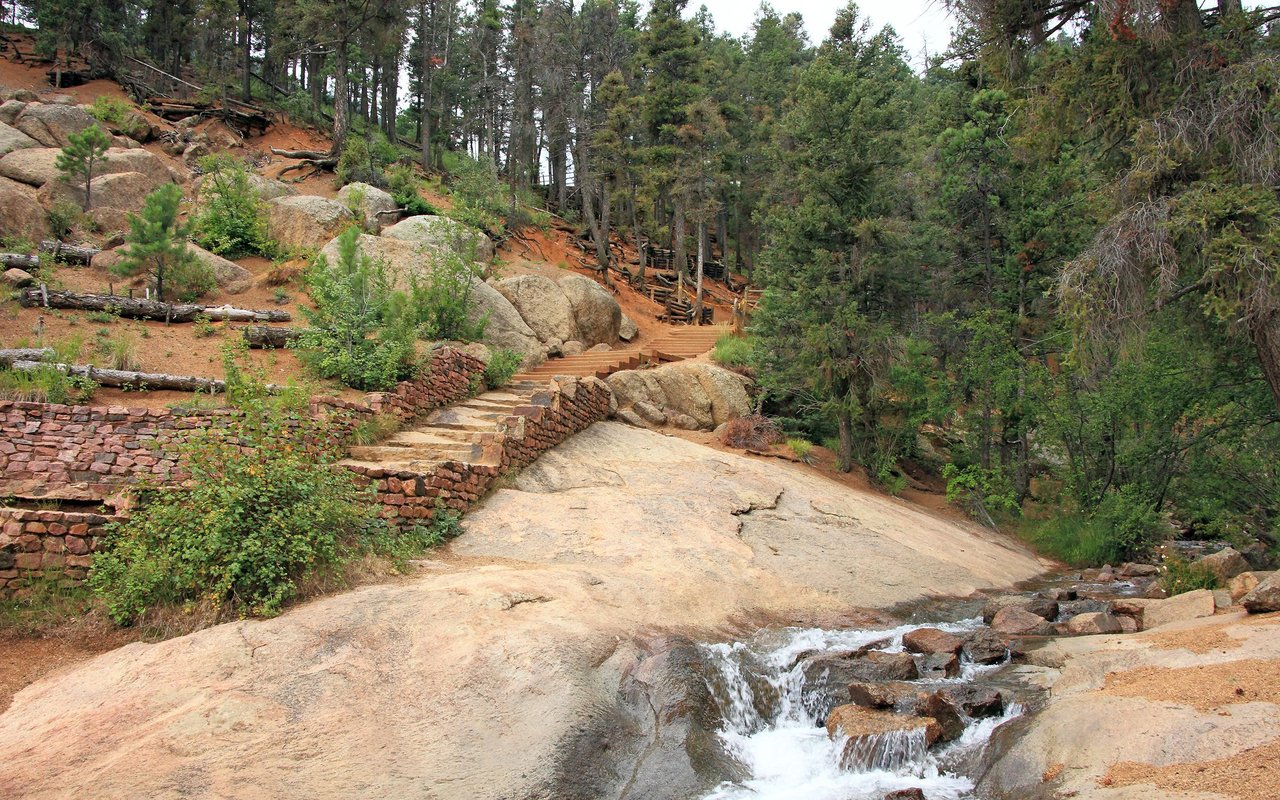 Rocky wooded trail with stone steps and a small cascading stream.