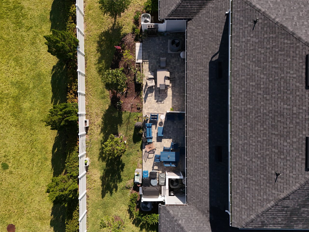 Aerial view of a home’s roof and paved backyard patio beside a fenced lawn.