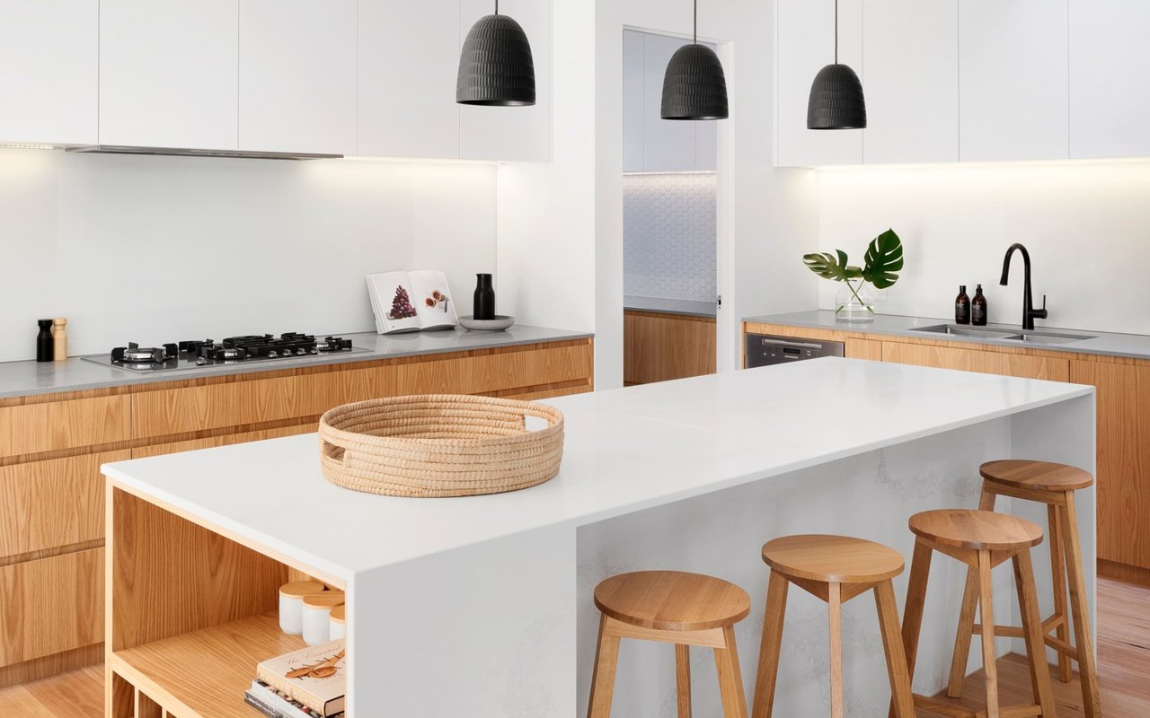 Modern kitchen with a large white island, warm wood cabinetry, and black pendant lights.