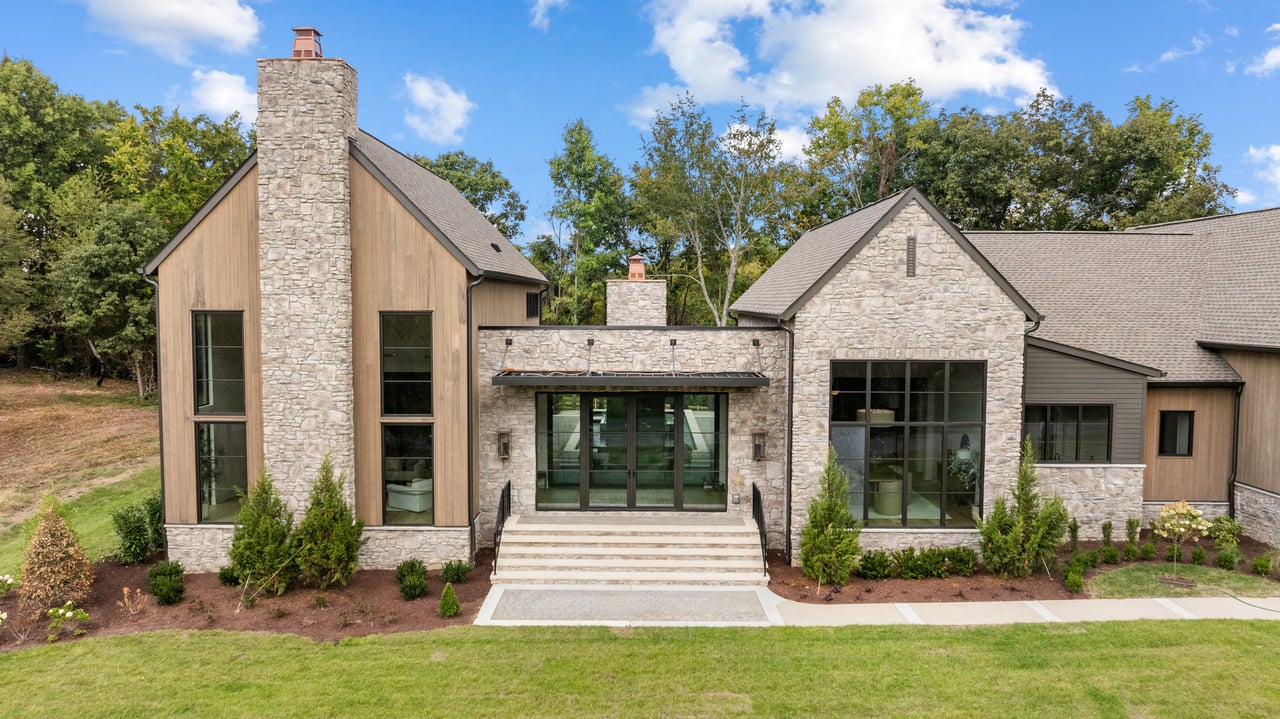 Modern stone-and-wood home with a prominent chimney and broad front entry steps.