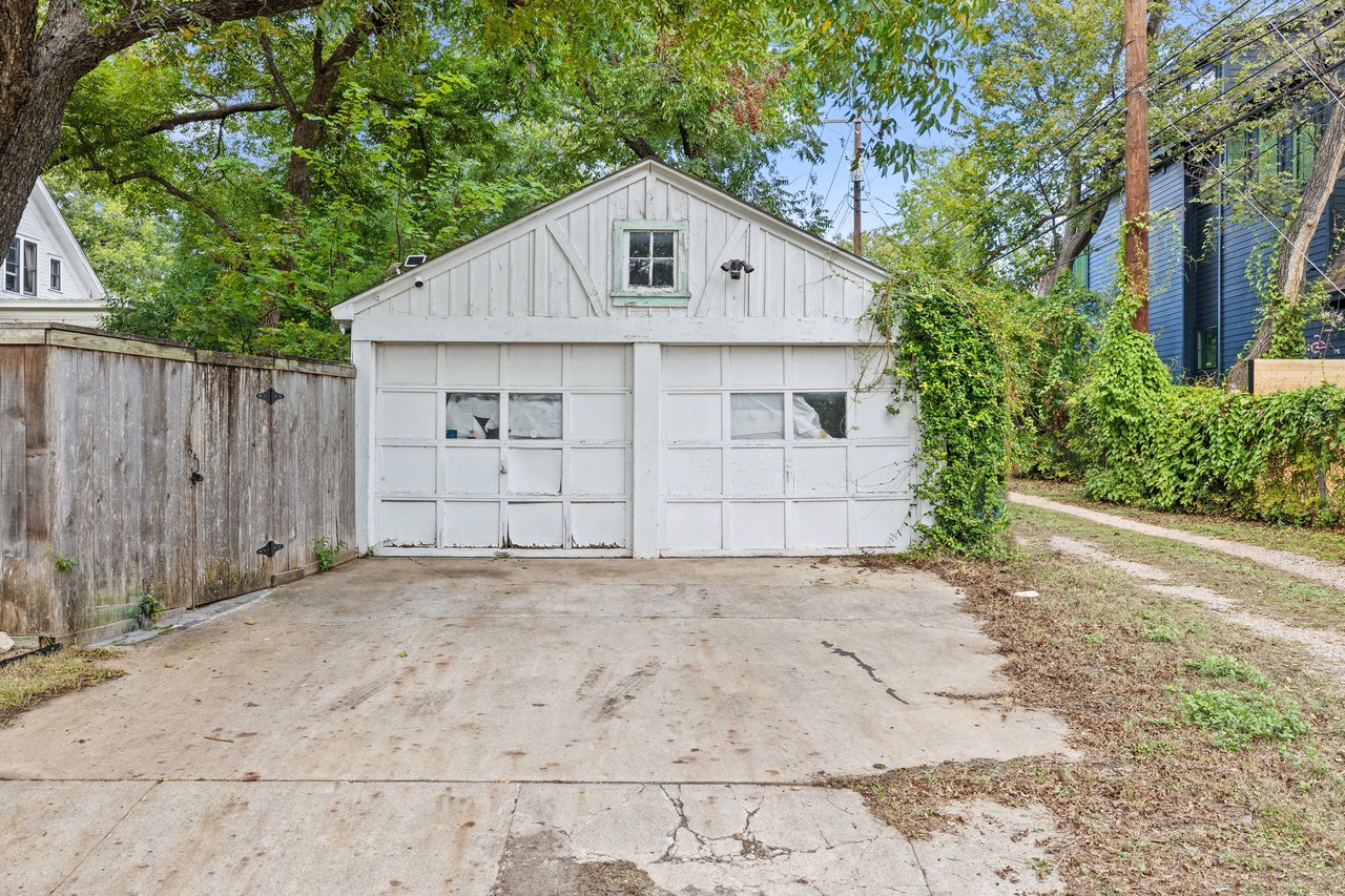 Detached white garage with two doors and a broad concrete driveway beneath mature trees.