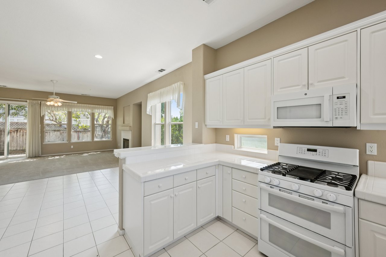 Kitchen with white cabinetry and gas range opens to a living area with a fireplace and sliding glass doors.