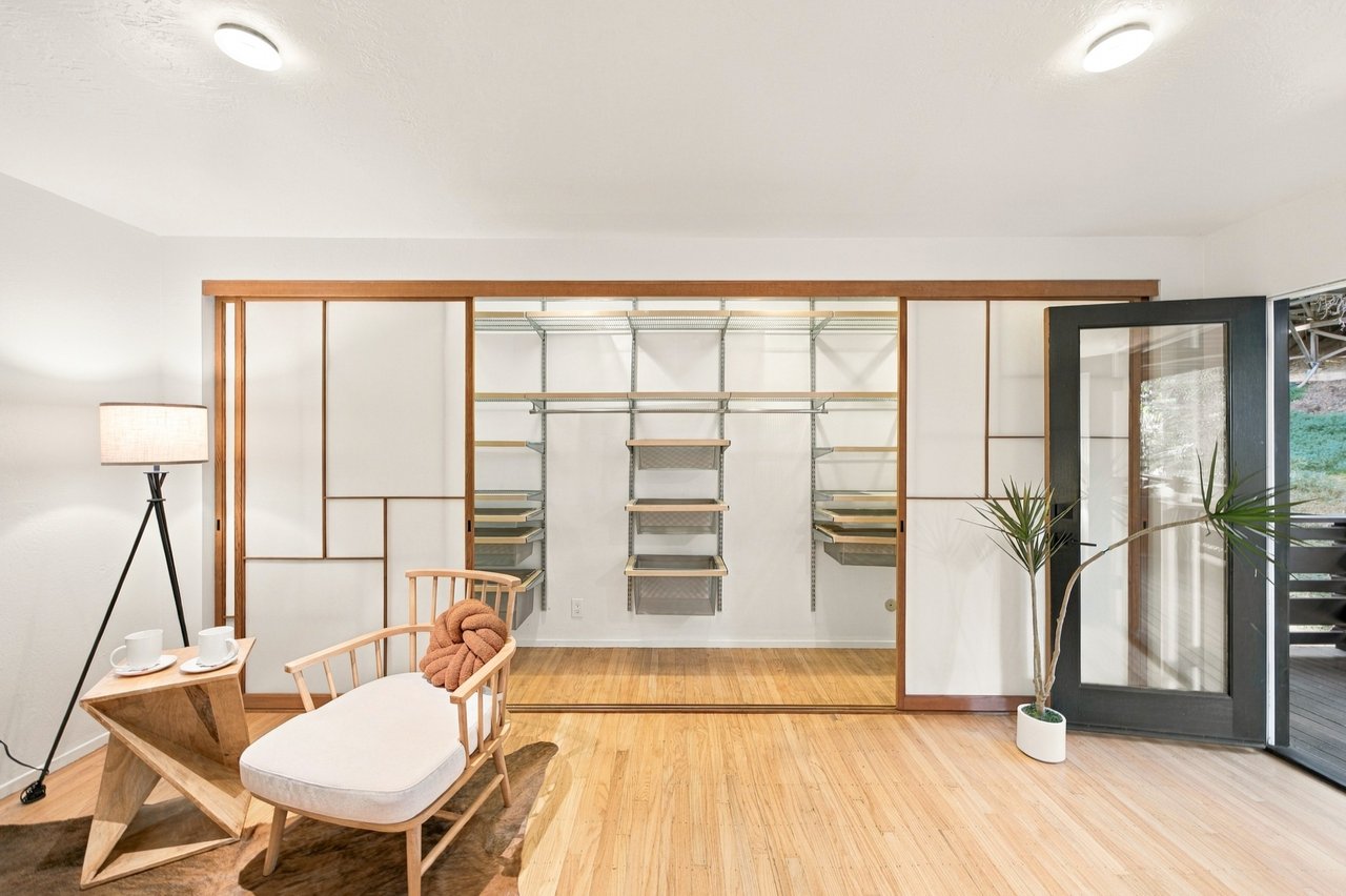 Dressing room with open shelving, sliding panels, and a wood-framed glass door.