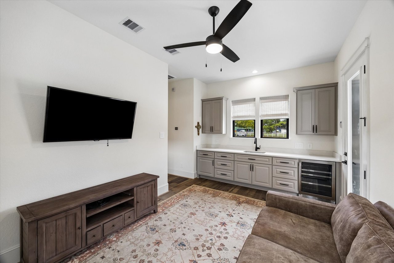 Furnished sitting room with a kitchenette, brown sofa, patterned rug, and wall-mounted television.