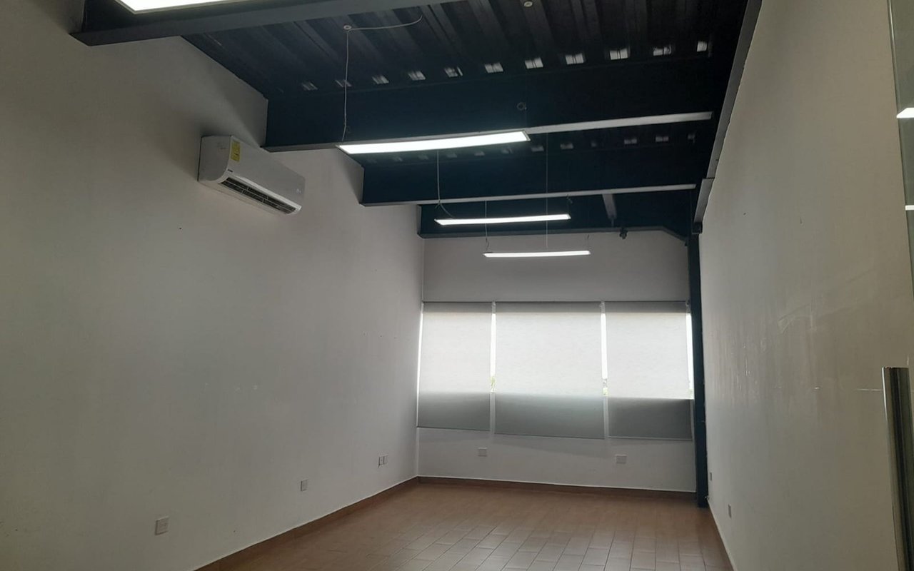Vacant office with a dark exposed ceiling, fluorescent lights, and shaded windows.