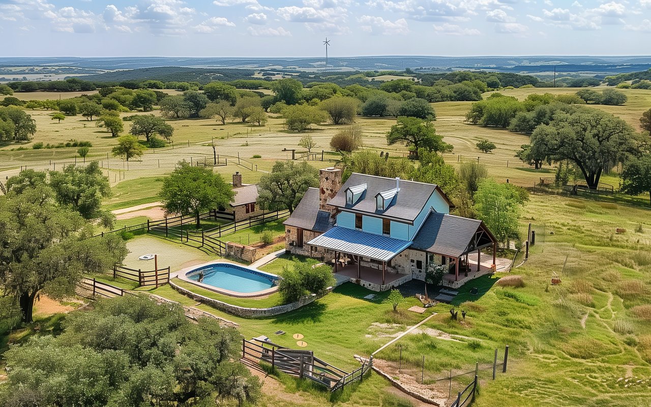 Aerial view of a country home with a swimming pool, fenced grounds, and rolling pastureland.