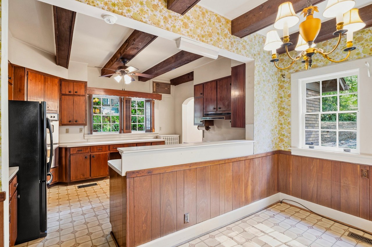 Kitchen with dark wood cabinets, exposed ceiling beams, patterned tile floor, and a long peninsula.