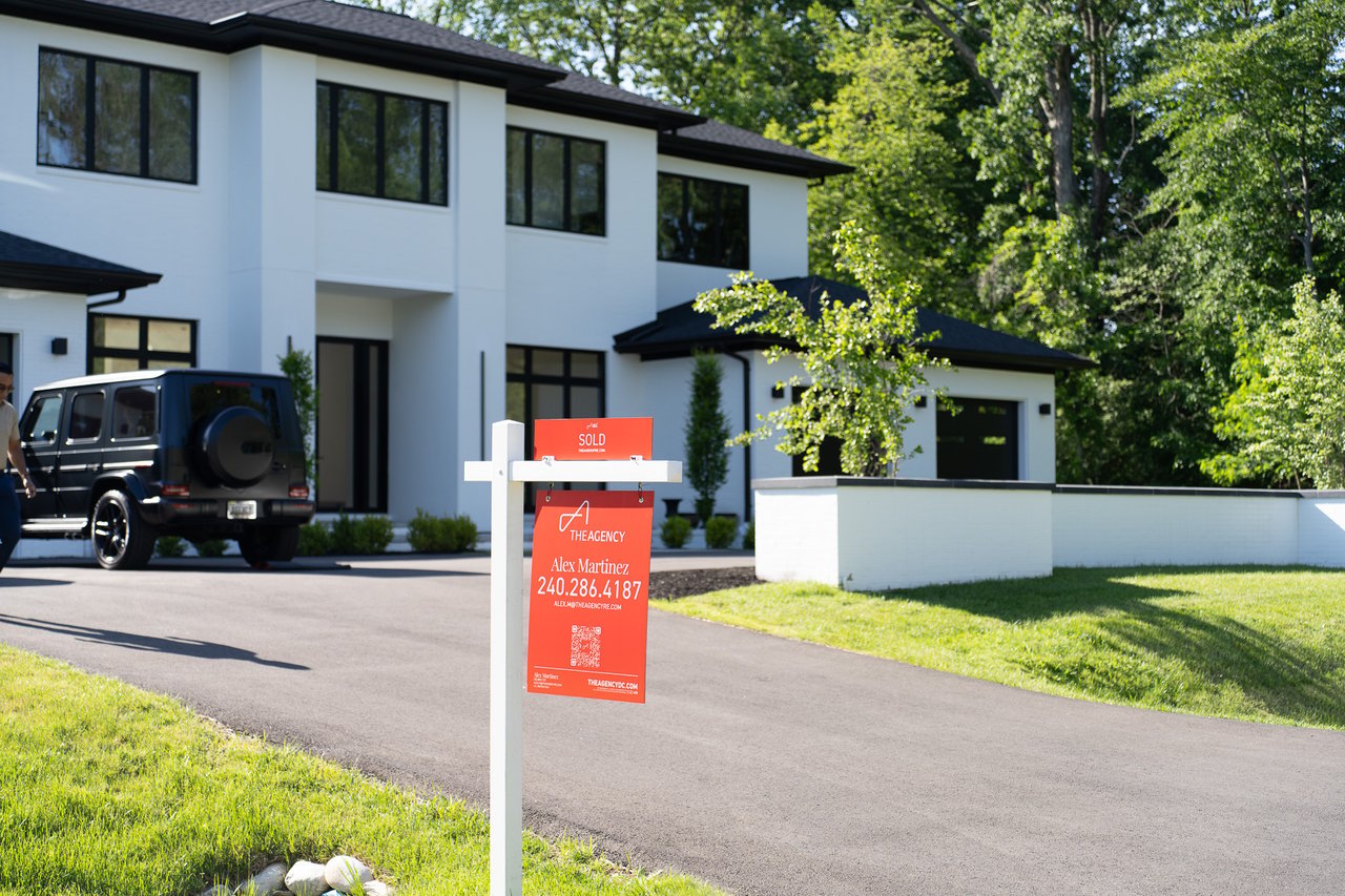 Modern white two-story home with black-framed windows and a red sold sign at the driveway.