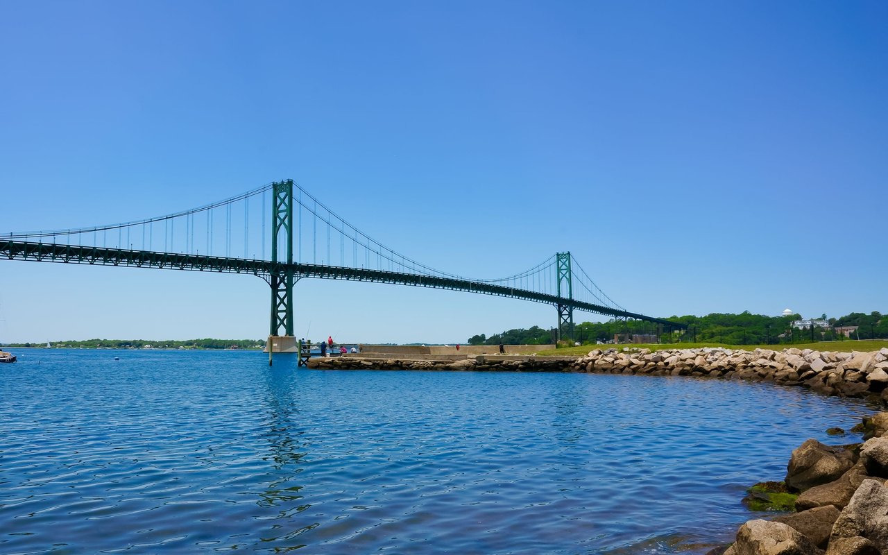 Mount Hope Bridge spans blue water beside a rocky shoreline.