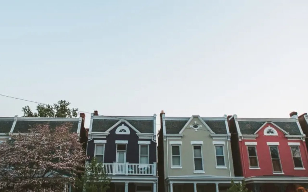 Three attached homes with ornate gables and porches in navy, pale green, and red.