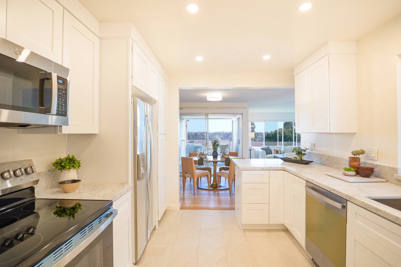 Bright modern kitchen at 6321 Caminito Luisito in San Diego, CA 92111, featuring white cabinetry, stainless steel appliances, quartz countertops, and open layout leading to dining and living room with natural light.