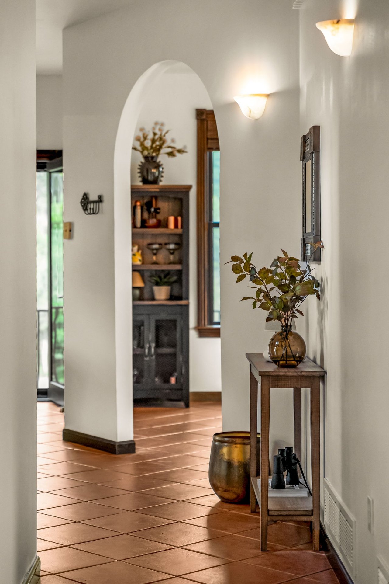 Hallway with terracotta tile floors, an arched doorway, and a console table topped with leafy branches.