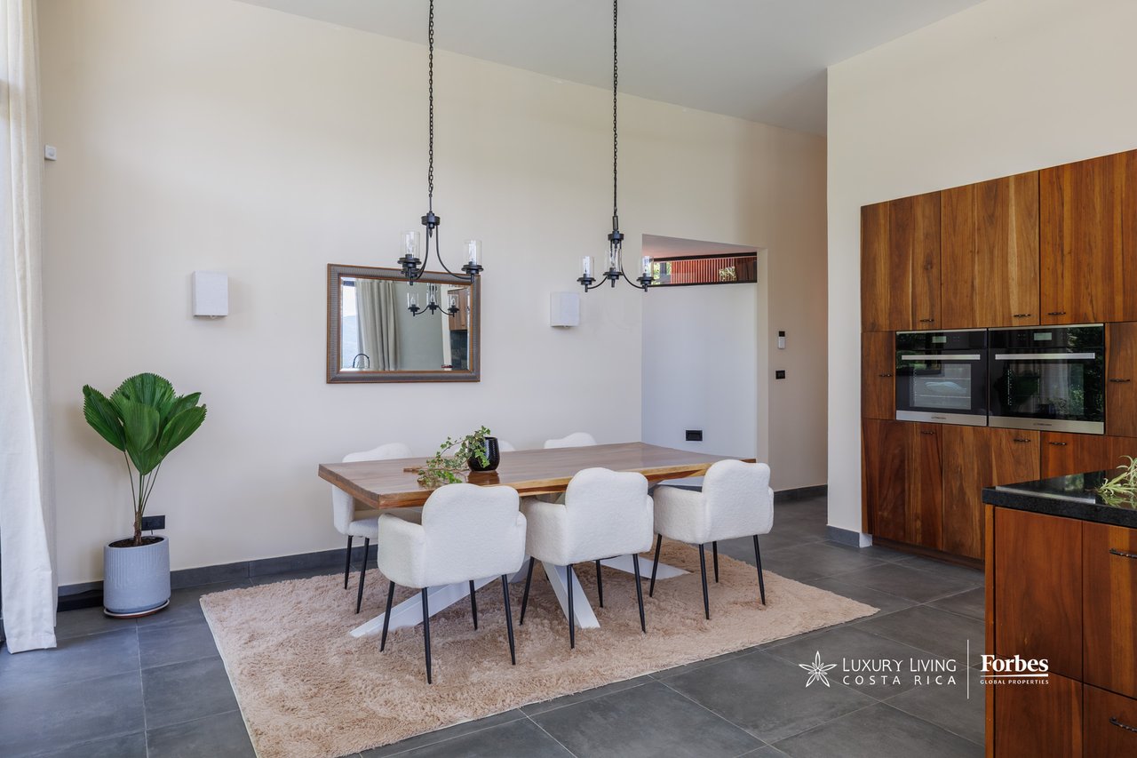 Dining area with a wooden table, white chairs, and walnut kitchen cabinetry.
