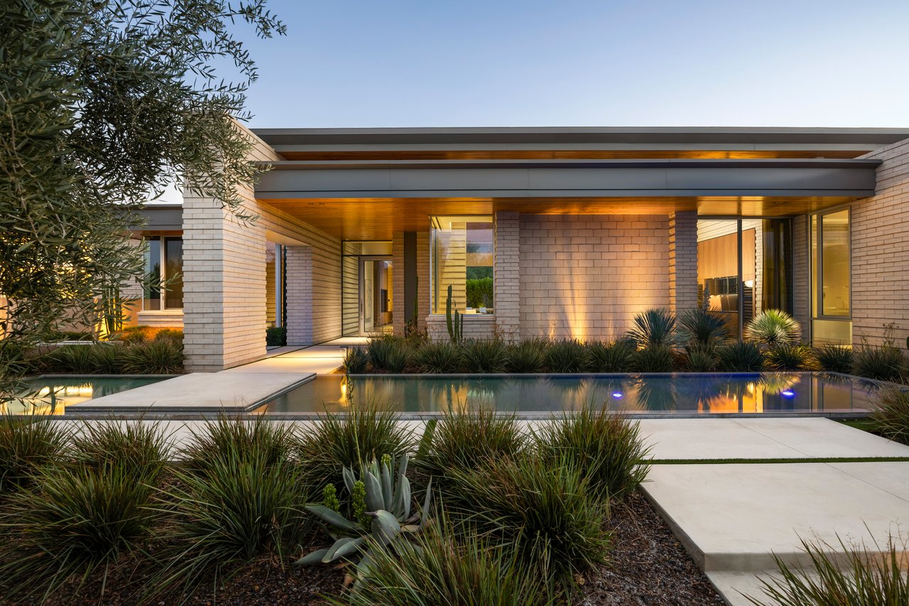 Modern home with a swimming pool, pale brick exterior, and desert landscaping at golden hour.