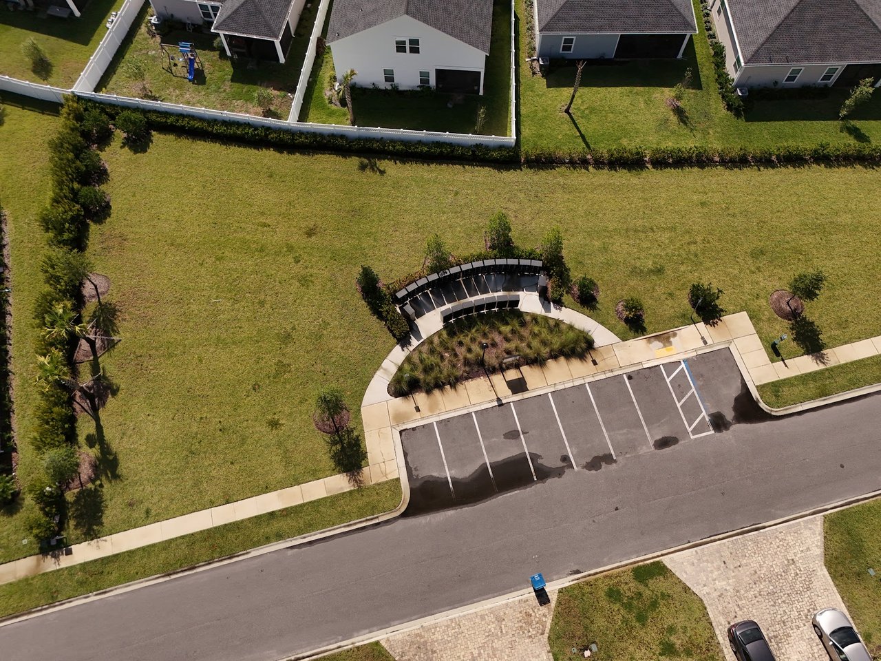 Aerial view of a neighborhood green with a curved bench, walking paths, and adjacent parking spaces.