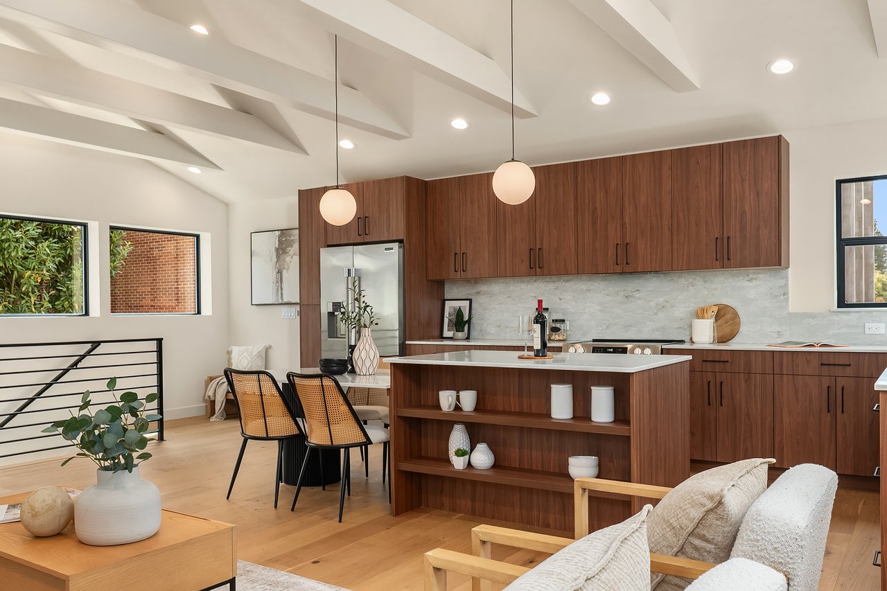 Open-plan kitchen with walnut cabinetry, a large island, and adjoining lounge beneath exposed ceiling beams.