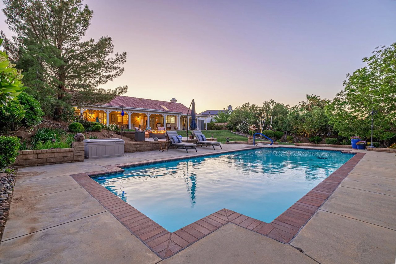 Backyard swimming pool with a raised spa, patio loungers, and a covered outdoor living area at dusk.