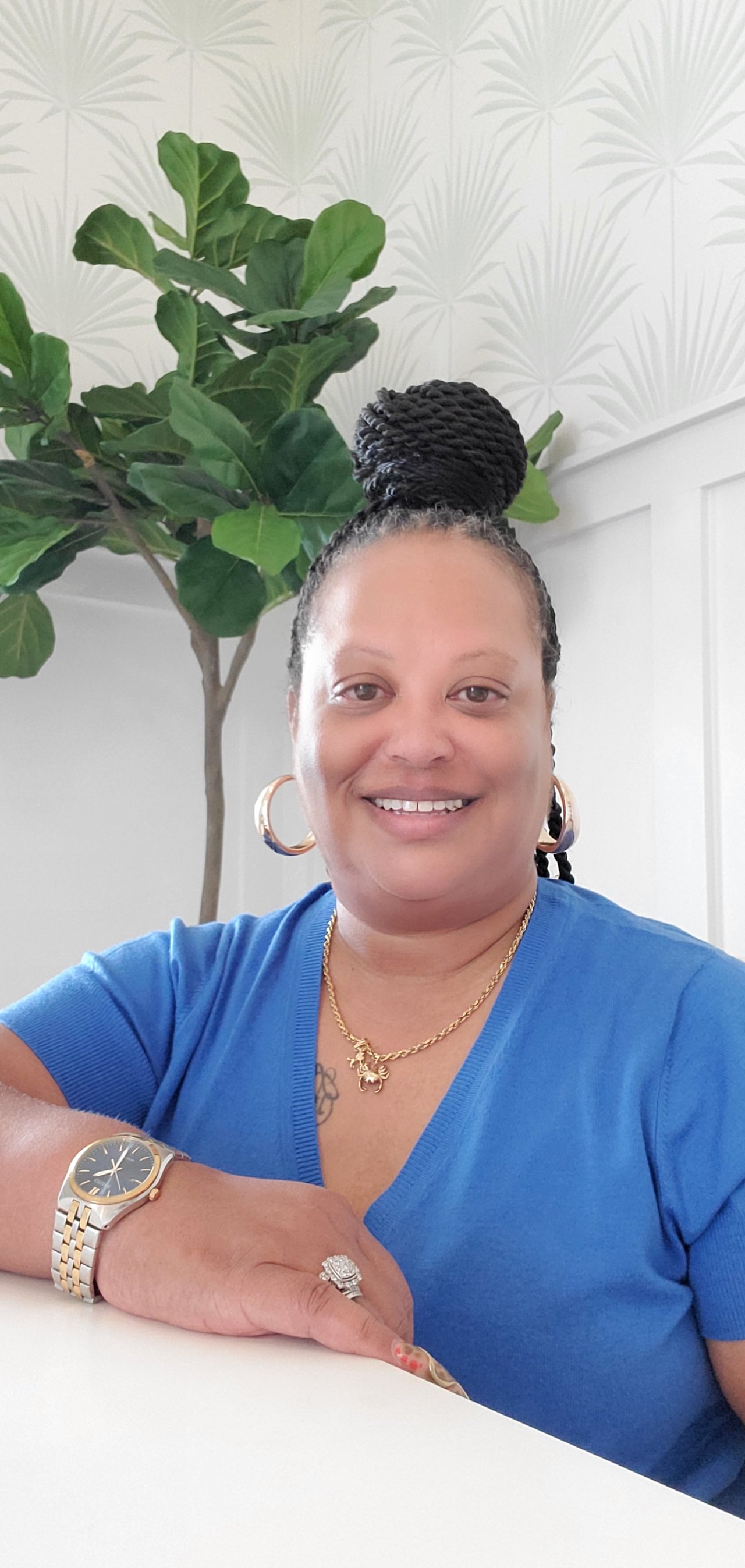 Enreicka Alston smiling in a blue top beside a leafy indoor plant.