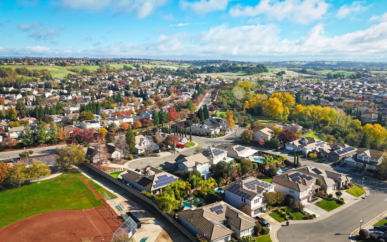 Aerial view of Harbor City homes and tree-lined streets, with a sports field in the foreground.