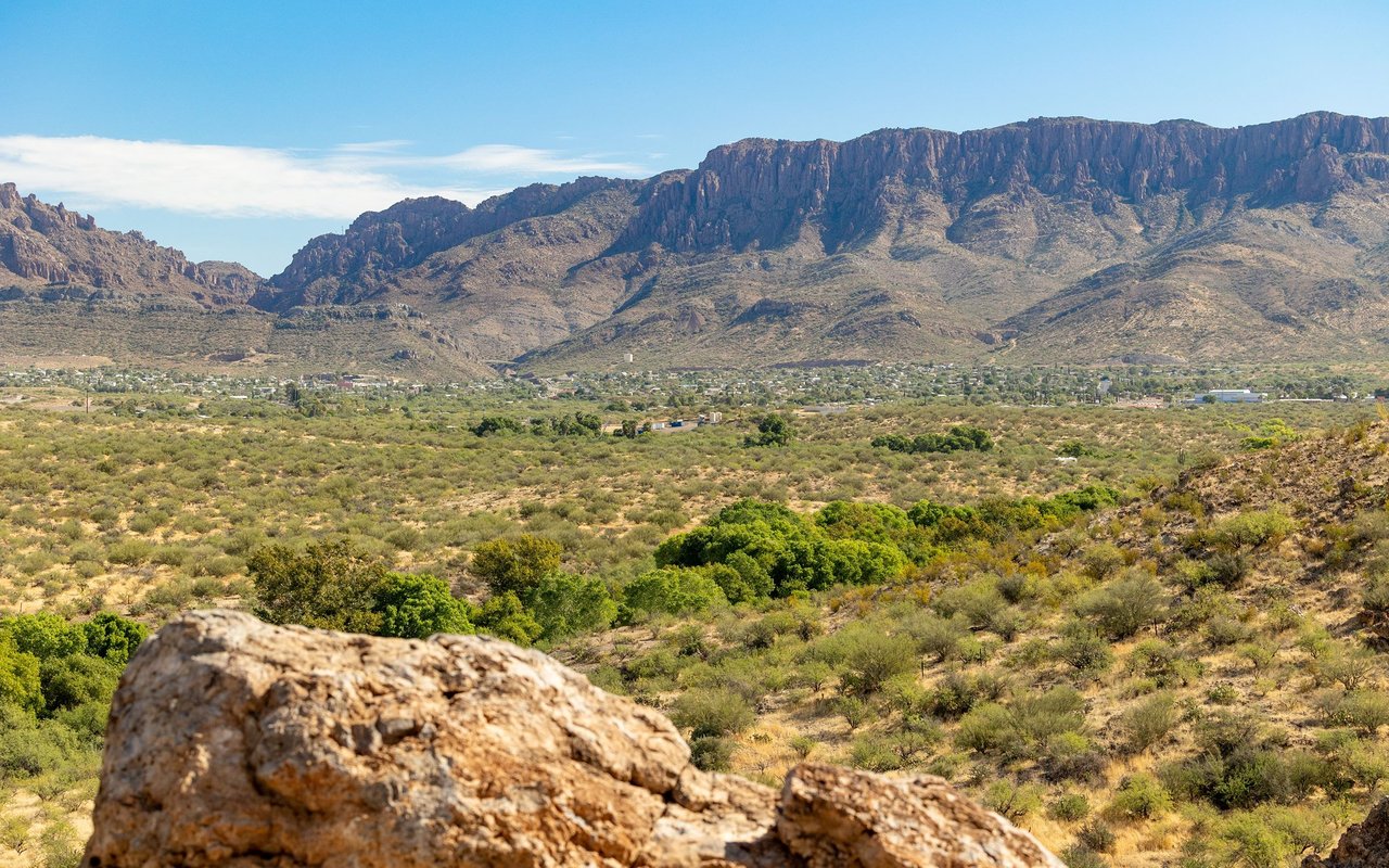 Desert valley and rugged mountains beyond scrubland, with large boulders in the foreground.