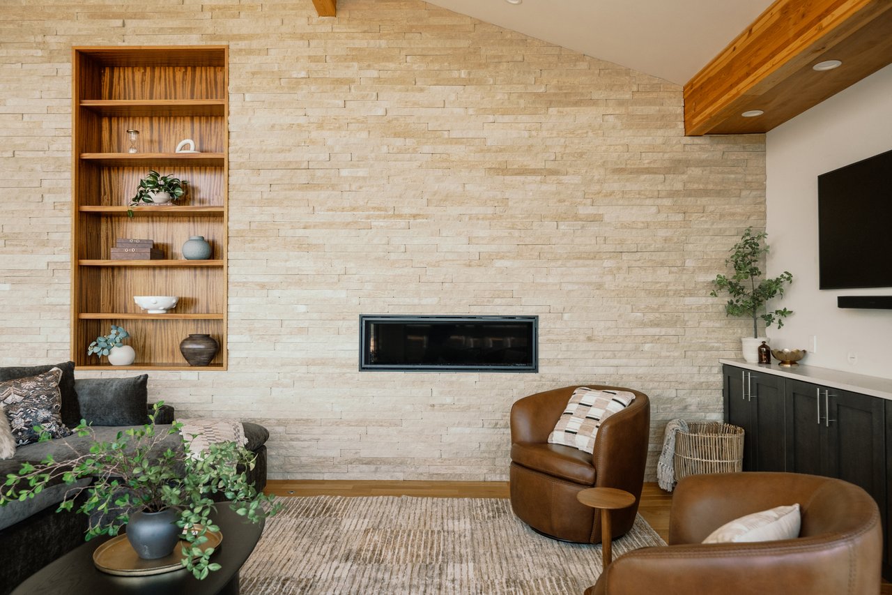 Living room with a stacked-stone feature wall, built-in shelving, linear fireplace, and leather armchairs.
