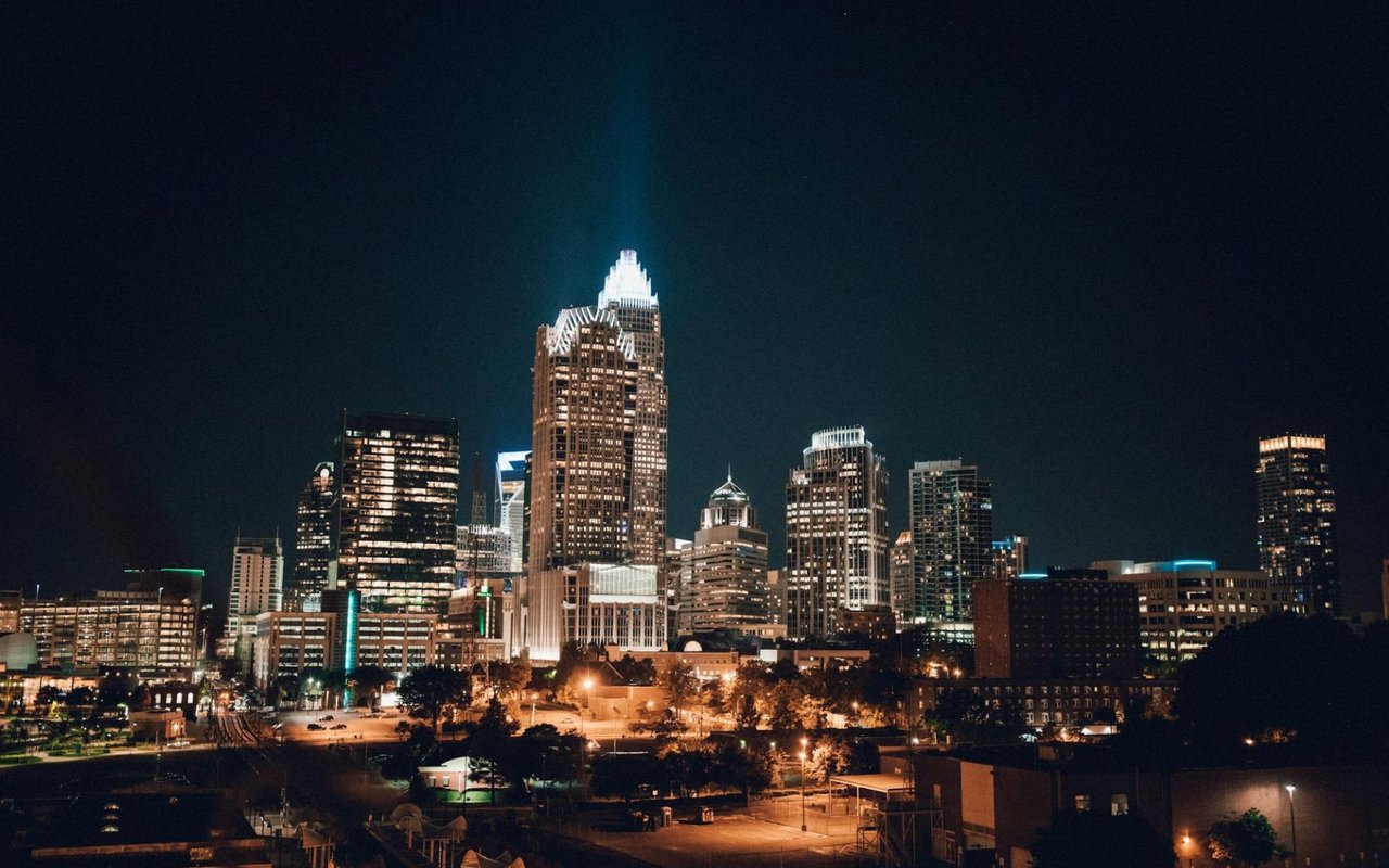  A striking night-time cityscape, likely Charlotte, North Carolina, with numerous illuminated skyscrapers against a dark sky.