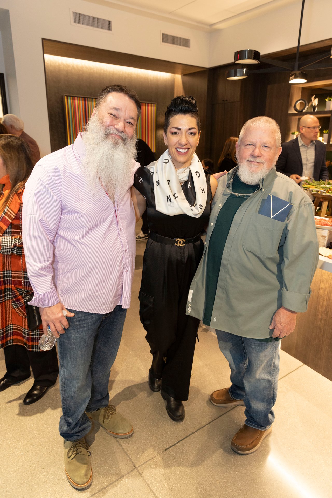 Three event attendees pose together indoors, including a woman wearing a white patterned scarf.