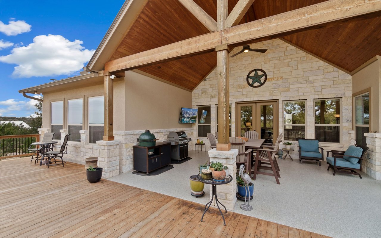 Covered patio with a timber ceiling, stone wall, outdoor kitchen, dining table, and wood deck.
