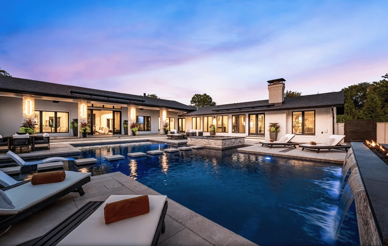 Modern home with a large pool, stone waterfall edge, and fire feature at dusk.