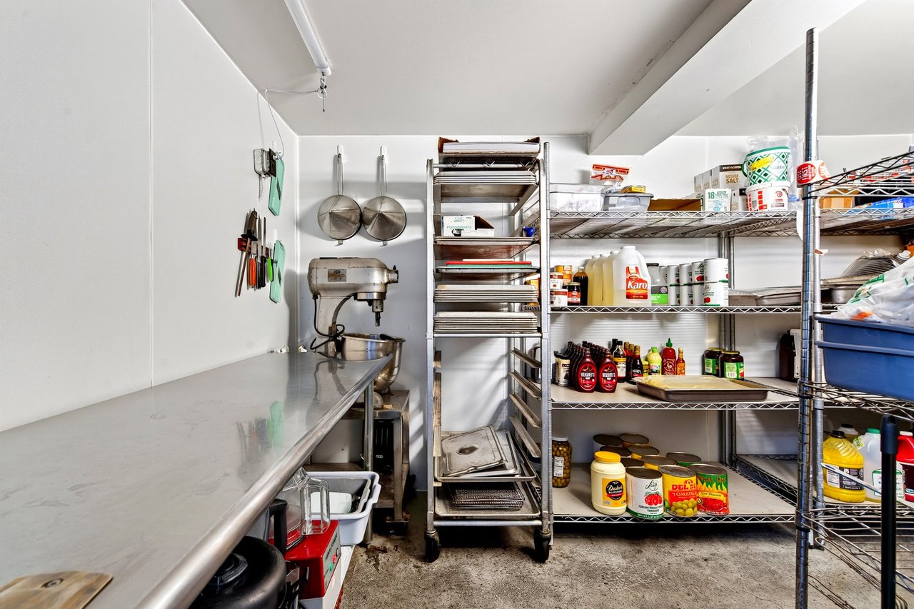 Restaurant kitchen pantry with stainless-steel counter, mixer, baking racks, and stocked shelves.