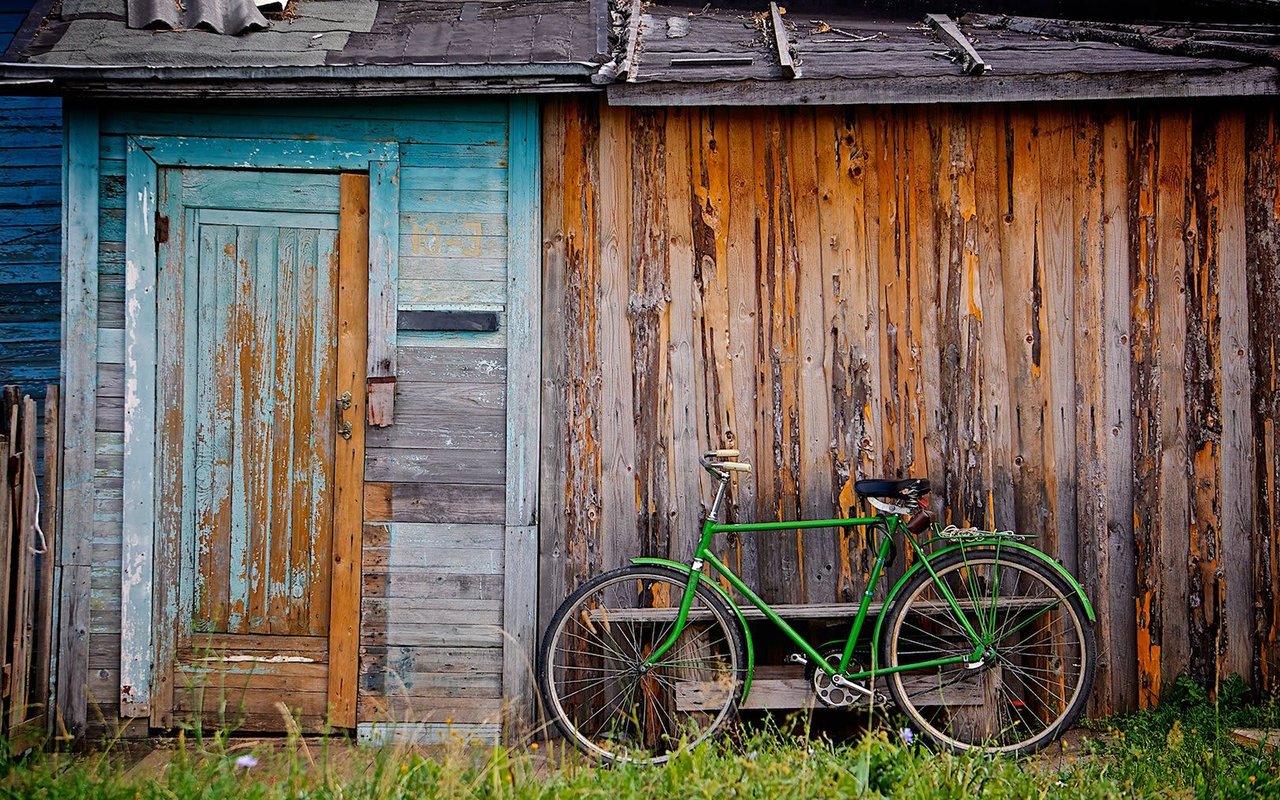 Weathered wooden shed with a turquoise door and green bicycle leaning against its wall.