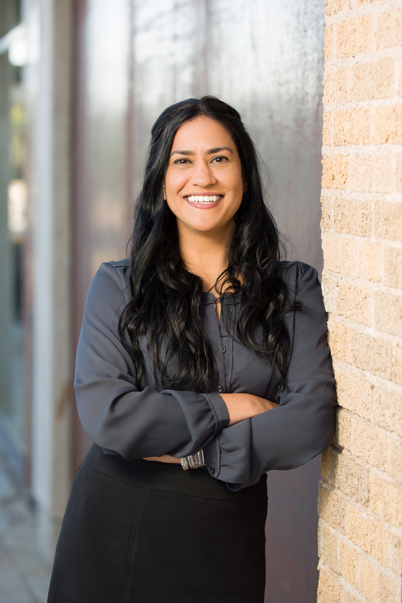 Sonia Allison smiling with her arms crossed beside a tan brick wall.