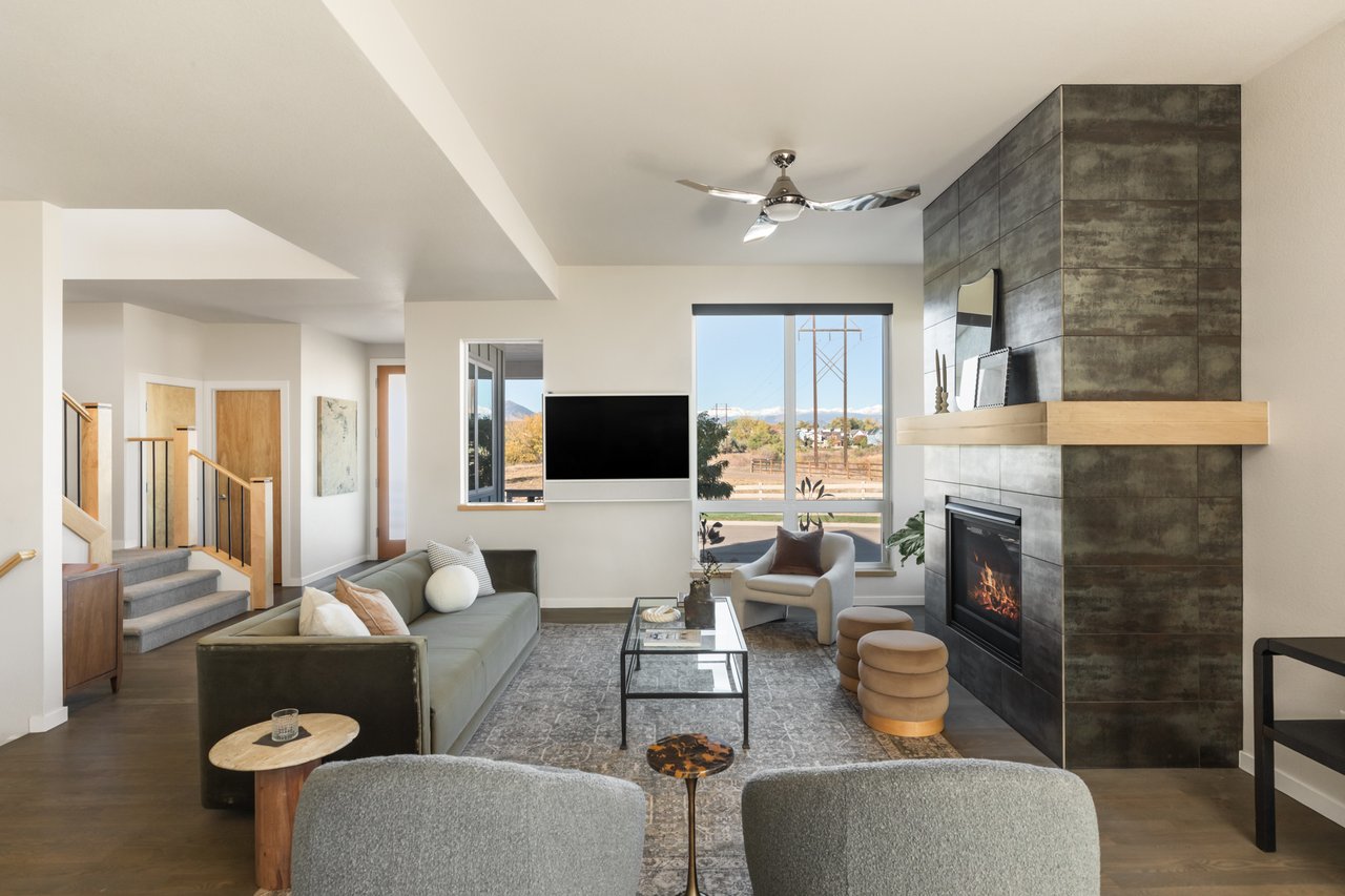 Living room with a sectional, wall-mounted TV, and fireplace, with the staircase to the left