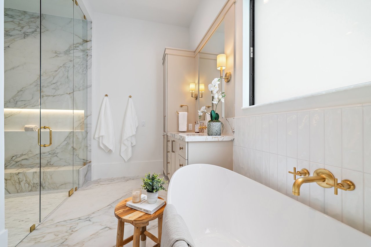 Luxury bathroom with a freestanding tub, marble glass shower, and gold fixtures.