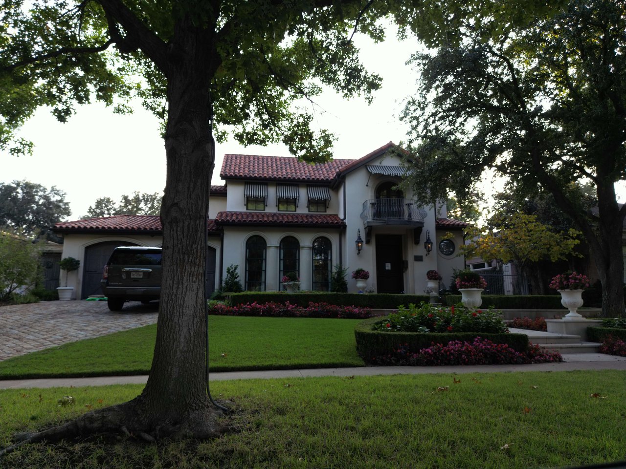 Two-story stucco house with a red tile roof, arched windows, and landscaped front yard.