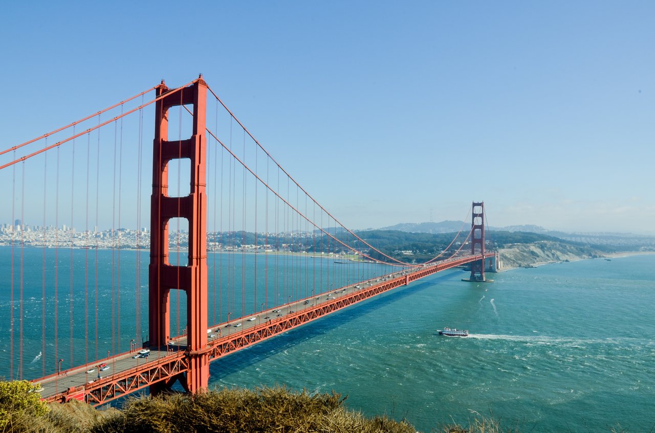 Golden Gate Bridge spans San Francisco Bay, with the city skyline and a boat in view.