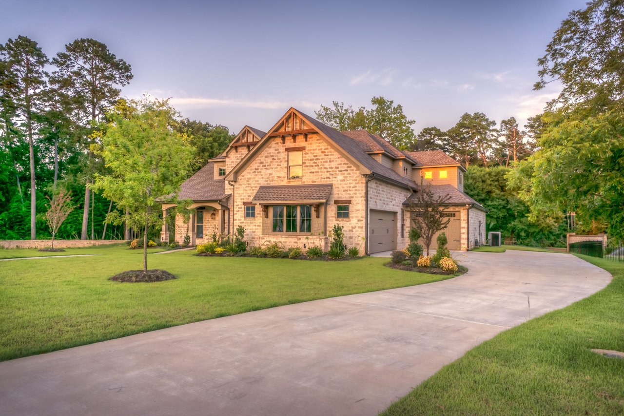 Limestone two-story home with gabled roof, green lawn, and mature oak and pine trees at golden hour.