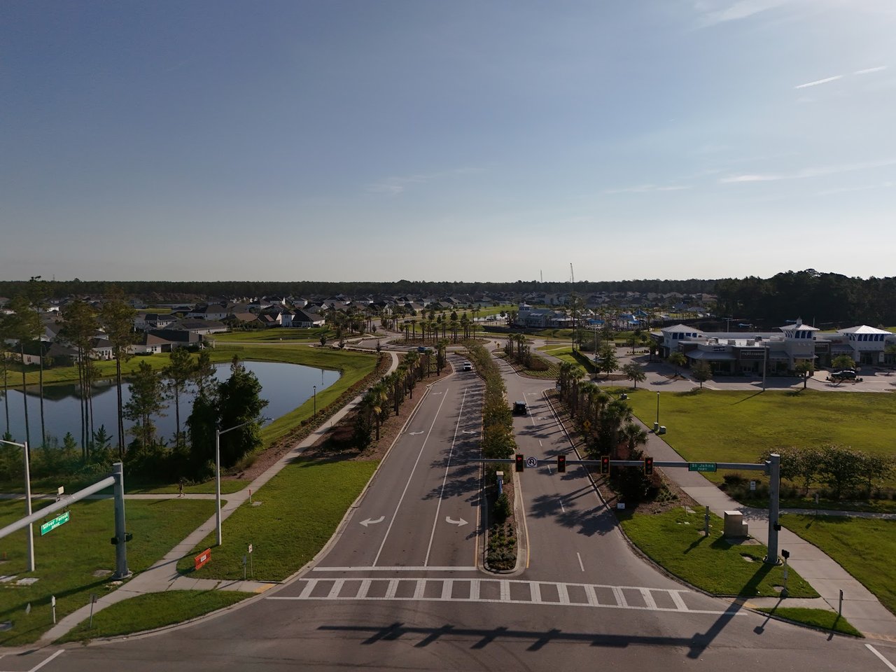 Aerial view of a residential community with a divided road, pond, and landscaped entrance.