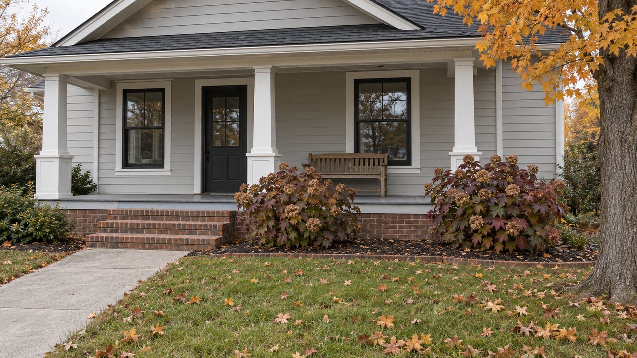 Light-gray gabled home with a covered porch, brick steps, and an autumn front garden.