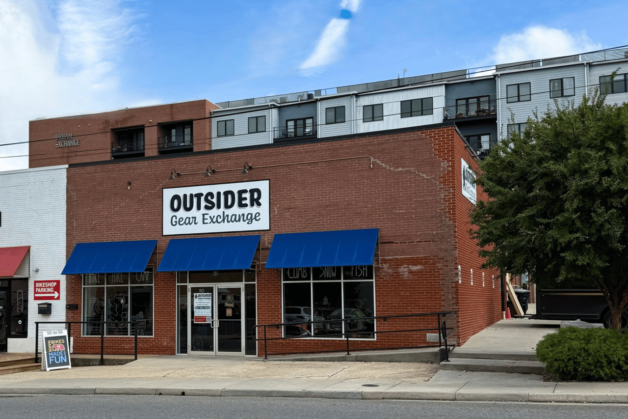 Outsider Gear Exchange storefront in a red-brick building with apartments above and blue awnings.