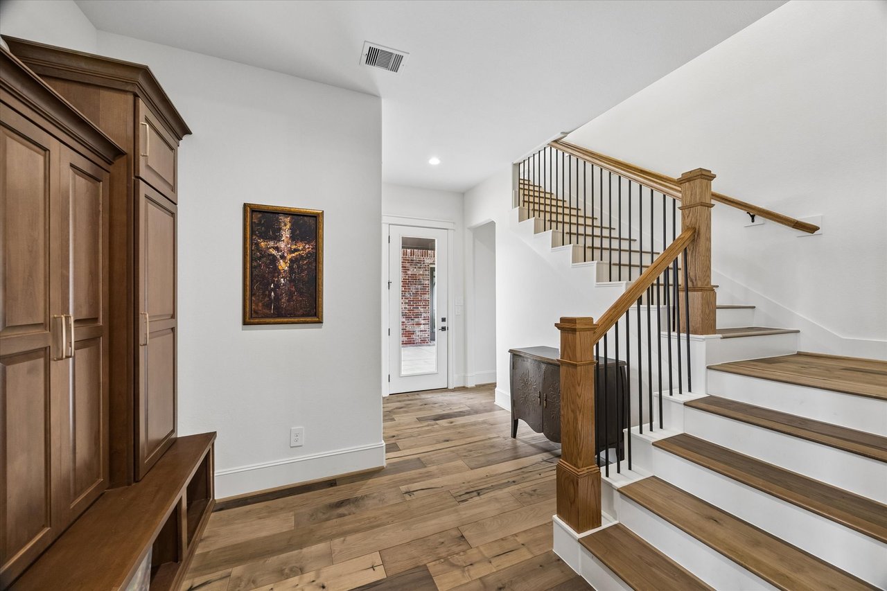 Foyer with a wood staircase, black metal balusters, and built-in cabinetry.