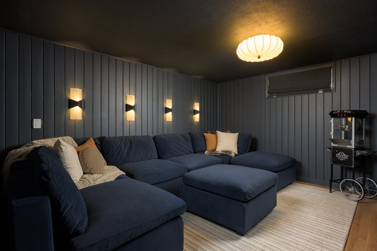Media room with a navy sectional, warm lighting, and a popcorn machine.